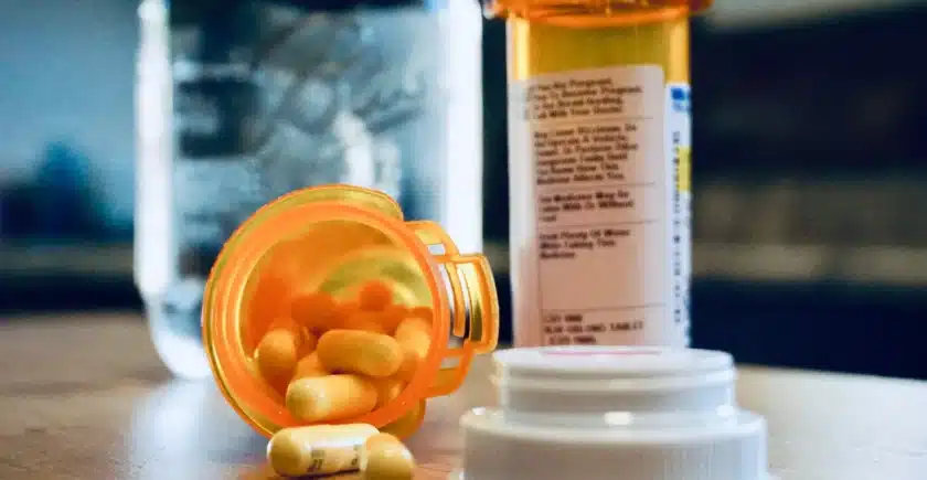 Prescription pill bottle spilled on a table with a glass of water in the background