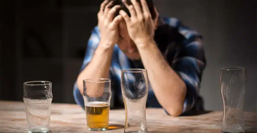 Man holding his head with his hands in front of two empty beer glasses. Binge drinking can lead to alcohol dependence